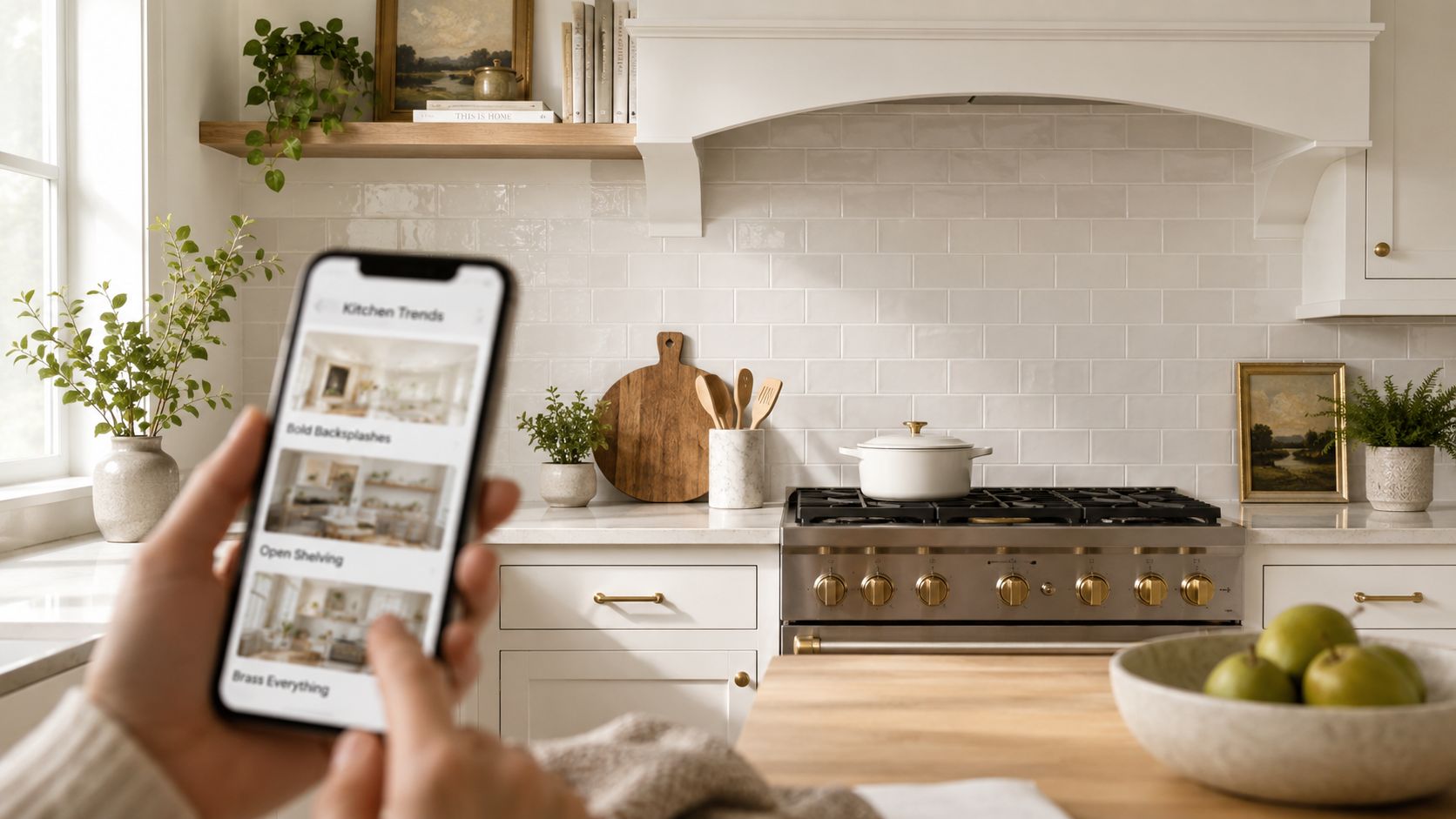 A person holding a smartphone showing kitchen design trends in front of a modern white kitchen.