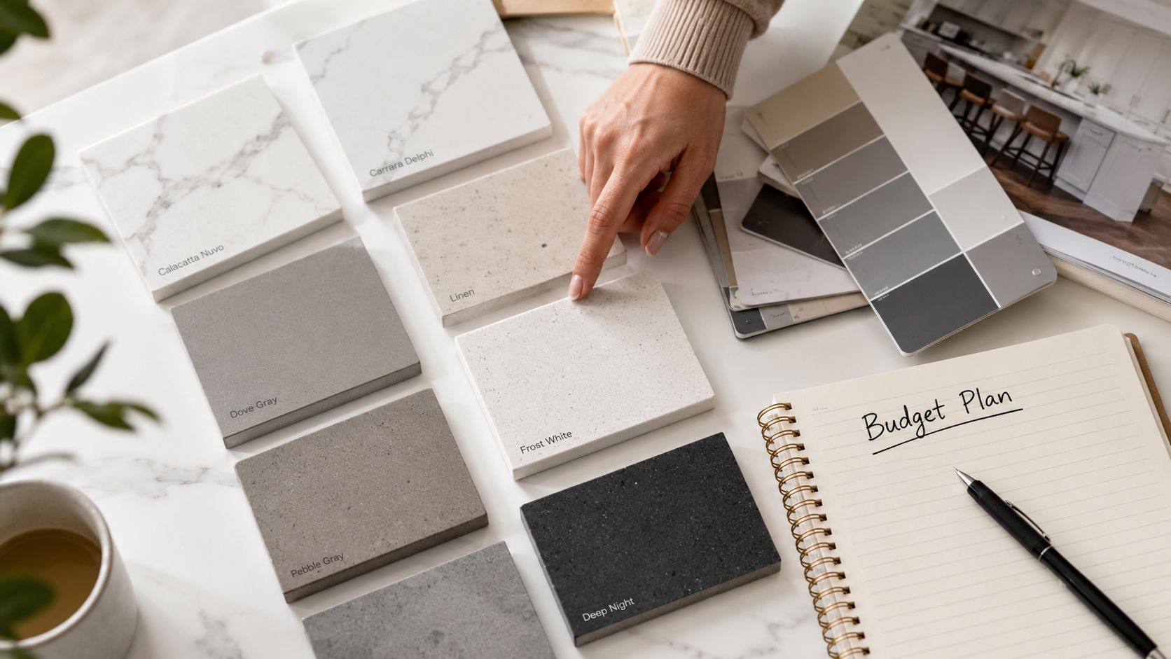 A designer's hand points to a sample of Frost White quartz countertop amidst various material finish samples.
