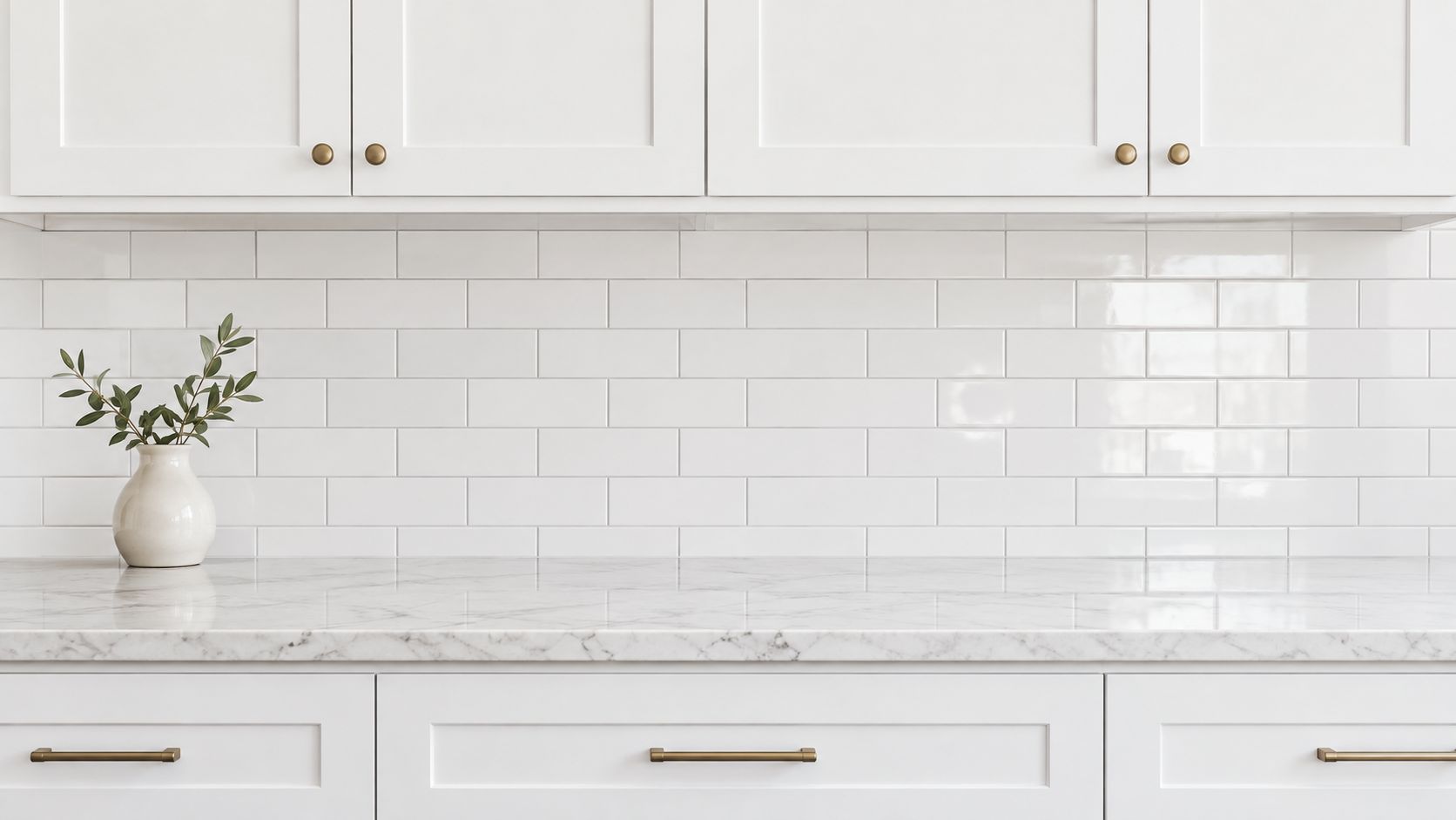 A modern kitchen interior featuring a clean white marble countertop and a classic white subway tile backsplash.